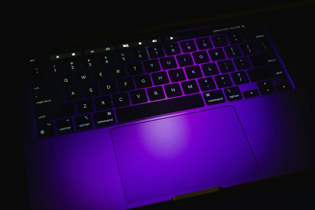 A laptop keyboard lit purple in the dark